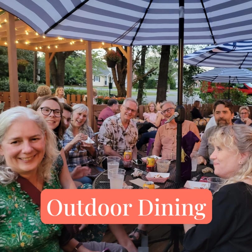 Smiling patrons enjoying outdoor dining under striped umbrellas and string lights at Succotash.