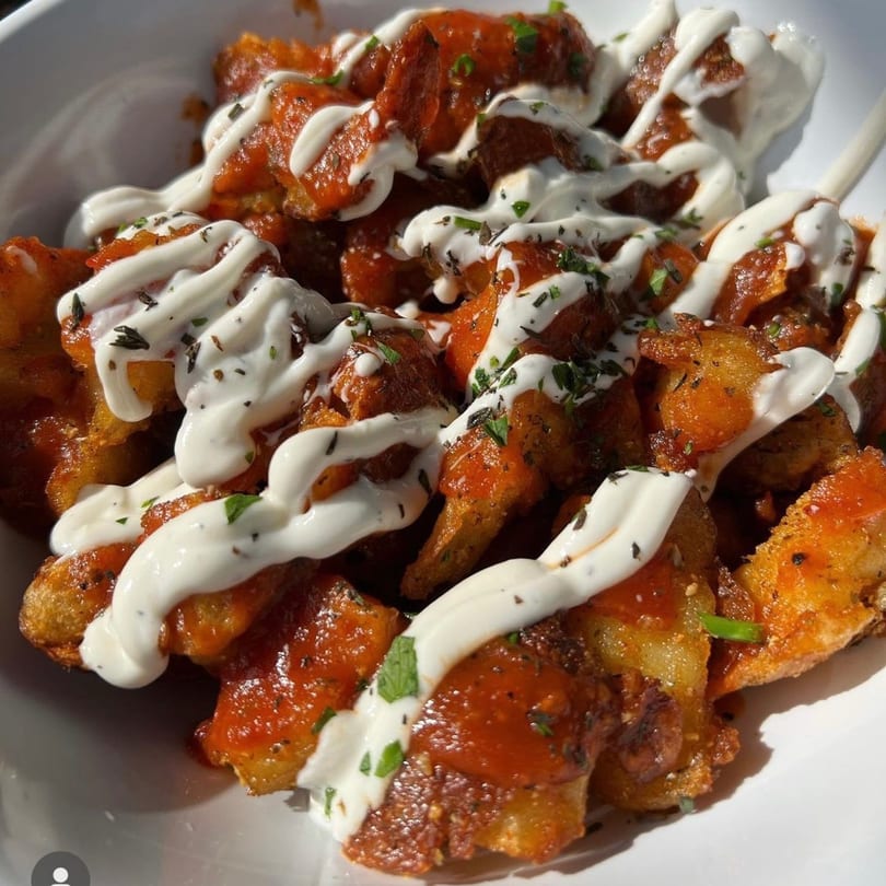 Crispy fried okra bites drizzled with white sauce, red sauce, and herbs in a white bowl.