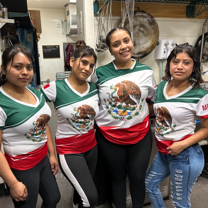 Four women in Mexican flag shirts pose in a commercial kitchen at Succotash Southern and Creole Kitchen.