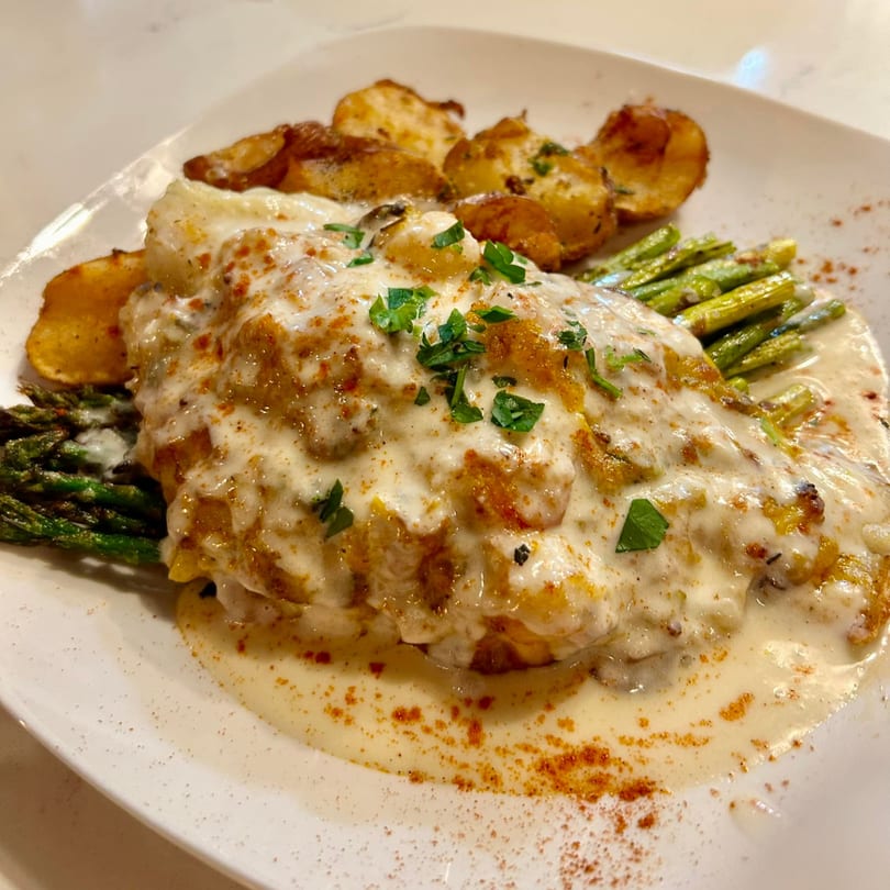 Succotash's creamy southern dish with chicken, roasted potatoes, and asparagus on a white plate.