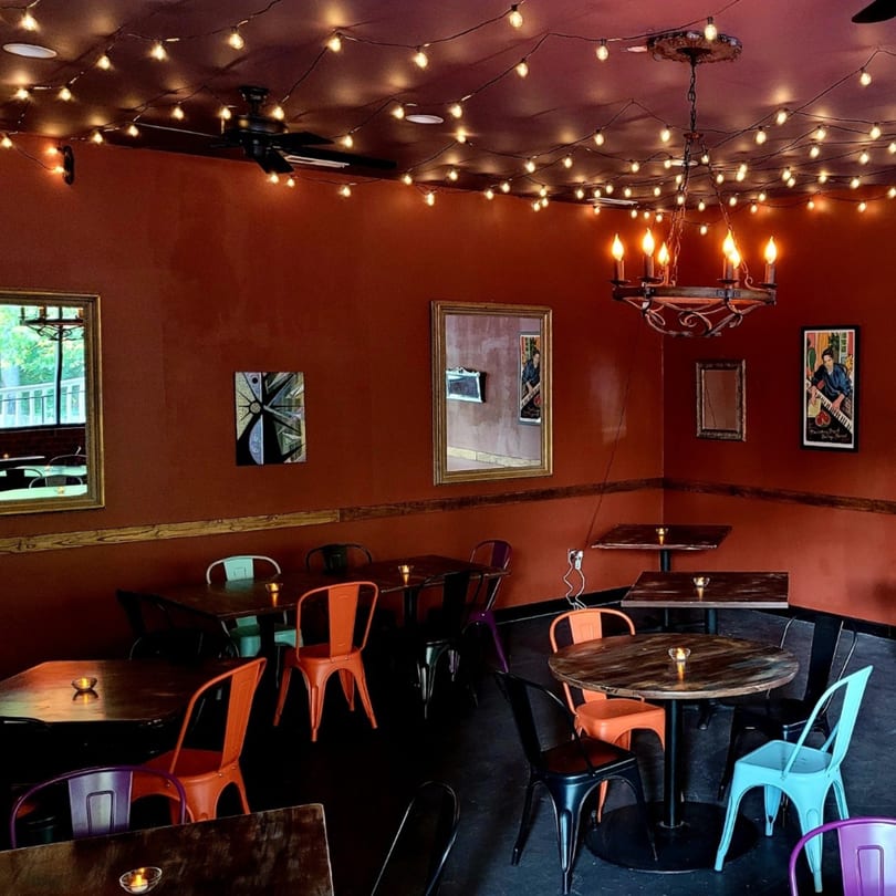 Warmly lit dining room at Succotash Southern and Creole Kitchen with string lights, mirrors, and colorful chairs.