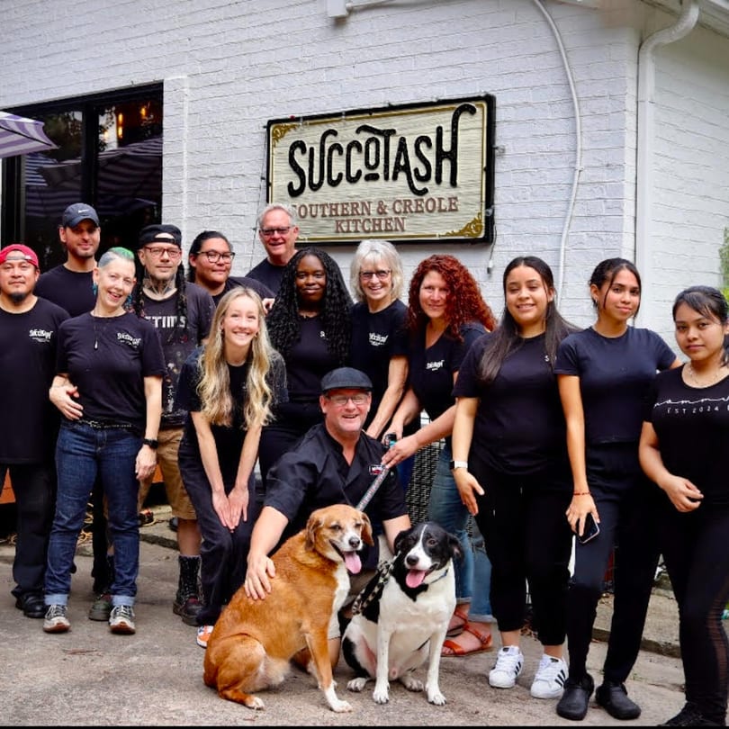 The Succotash Southern and Creole Kitchen team poses with two dogs in front of their restaurant.