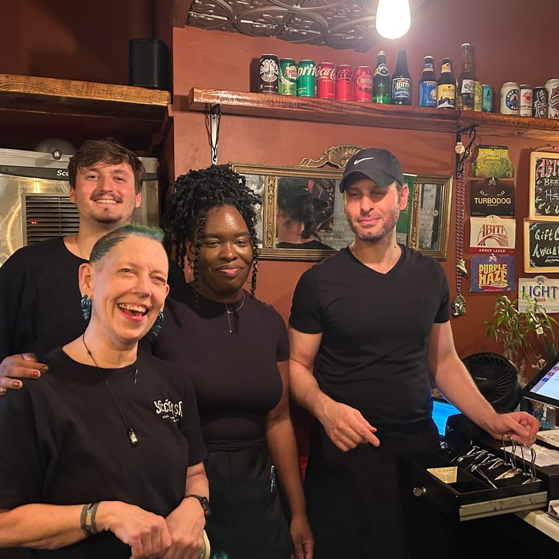 Four smiling Succotash Southern and Creole Kitchen staff members stand together behind the bar.