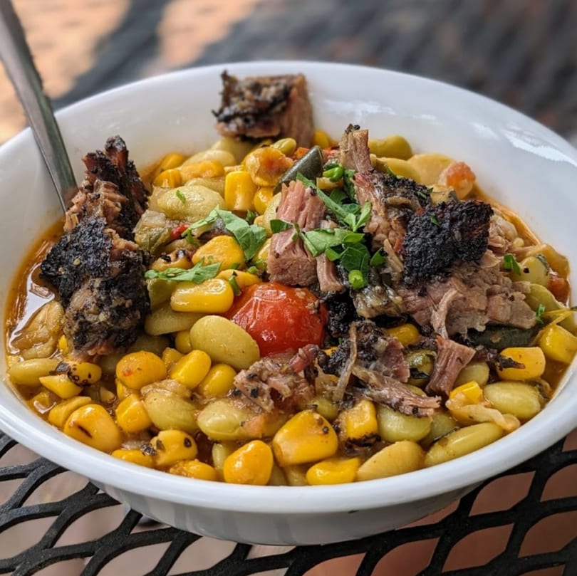Succotash dish with lima beans, corn, tomatoes, and shredded beef in a white bowl.